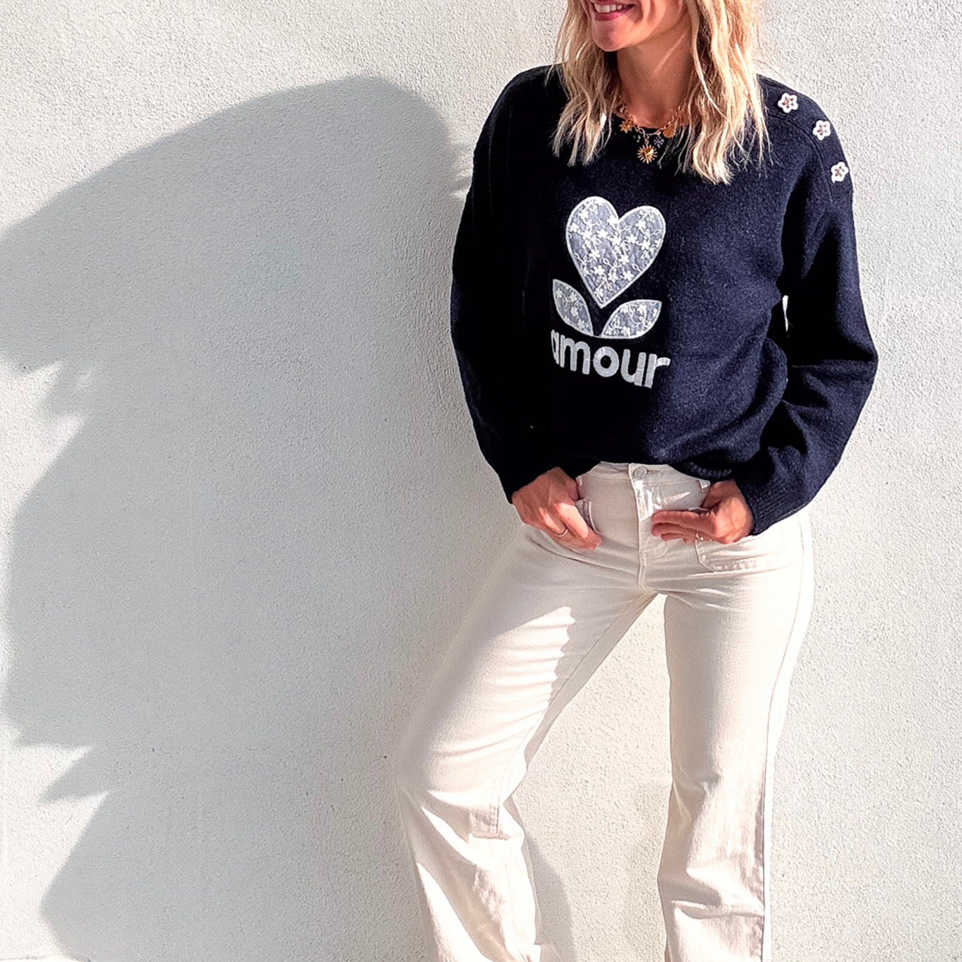 Pull bleu marine avec motif 'amour' cœur fleuri, boutons décoratifs sur l'épaule, porté avec un jean écru et des baskets blanches.