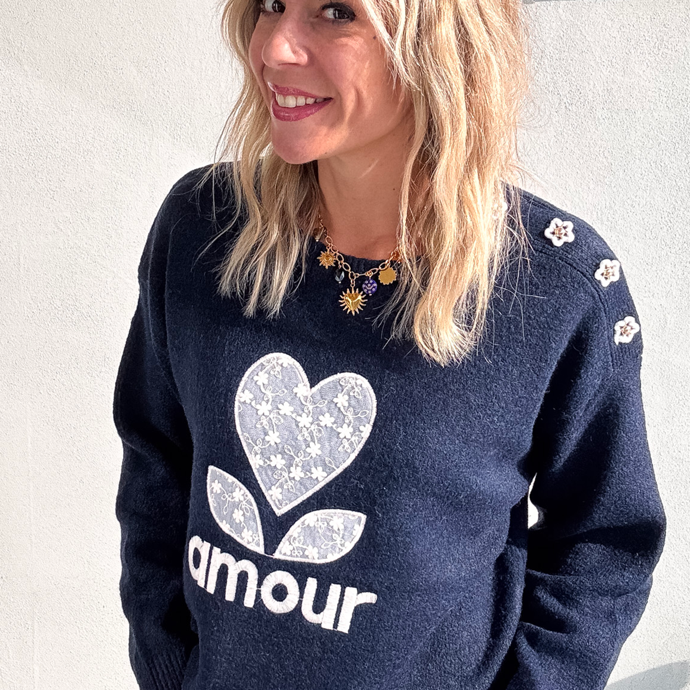 Pull bleu marine avec motif 'amour' cœur fleuri, boutons décoratifs sur l'épaule, porté avec un jean écru et des baskets blanches.