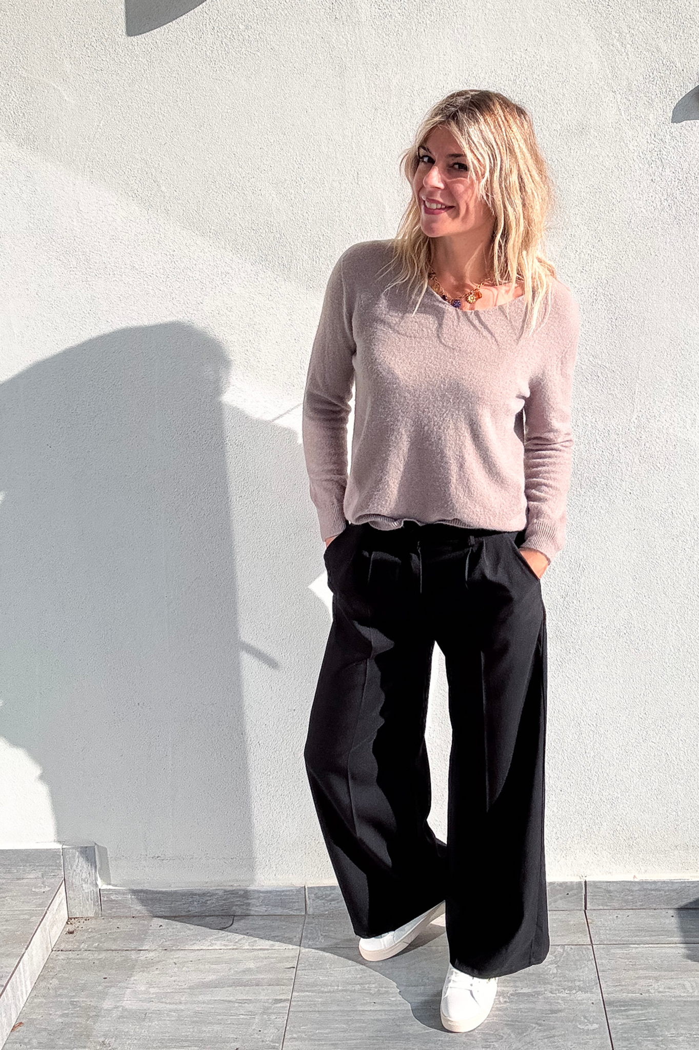 Pantalon large noir taille haute, coupe fluide, porté avec un pull taupe et des baskets blanches, look confortable et élégant.