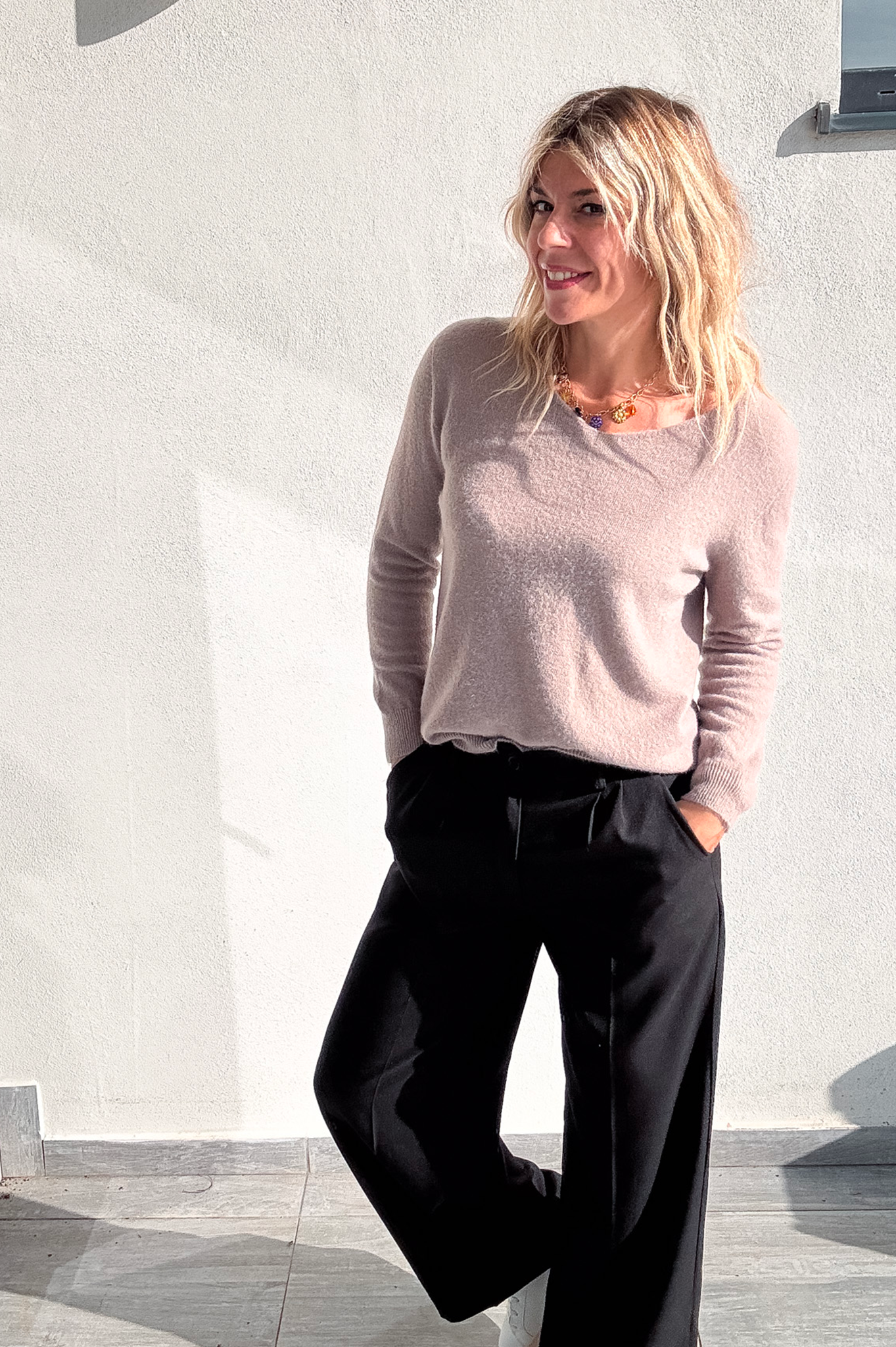 Pantalon large noir taille haute, coupe fluide, porté avec un pull taupe et des baskets blanches, look confortable et élégant.