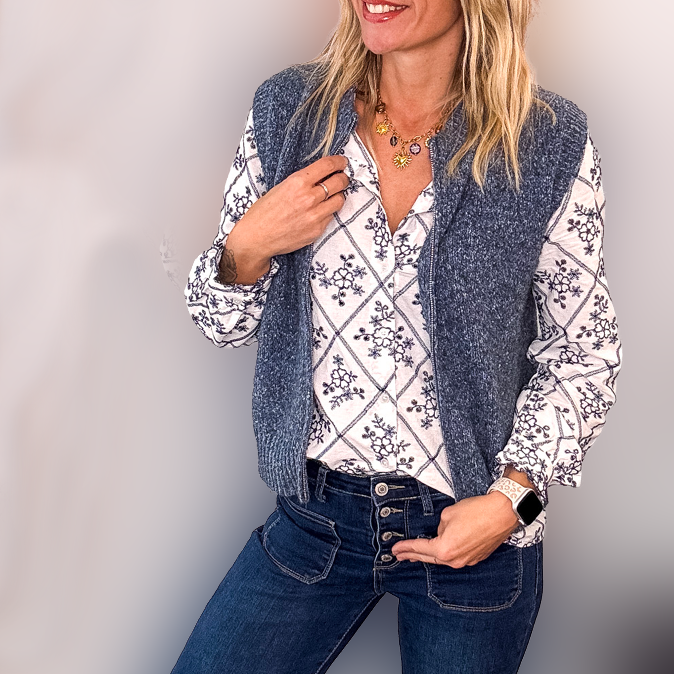 Gilet sans manches zippé bleu denim en maille tressée, col montant, porté sur une chemise à motifs et un jean flare.