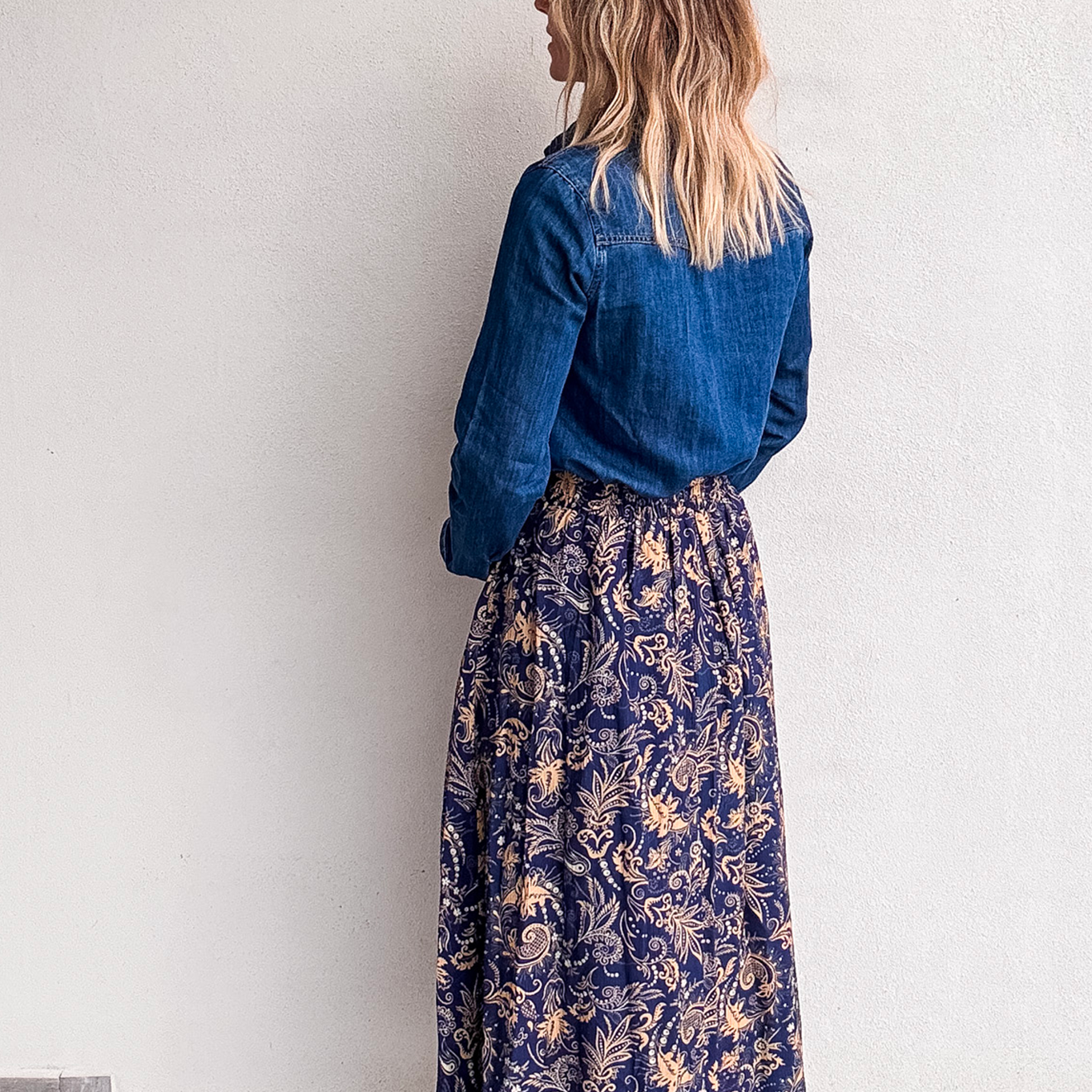 Jupe longue fluide motif cachemire bleu marine et or, portée avec une chemise en jean et des bottines noires.