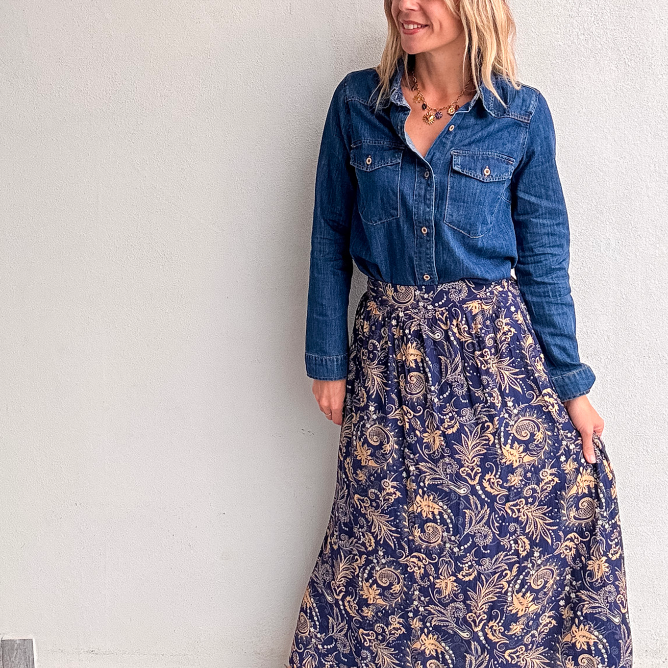 Jupe longue fluide motif cachemire bleu marine et or, portée avec une chemise en jean et des bottines noires.