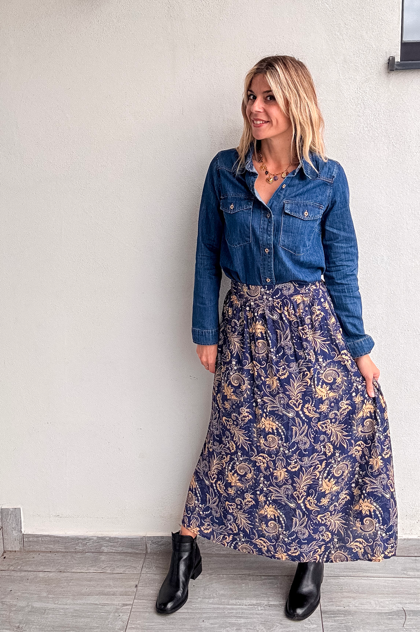 Jupe longue fluide motif cachemire bleu marine et or, portée avec une chemise en jean et des bottines noires.