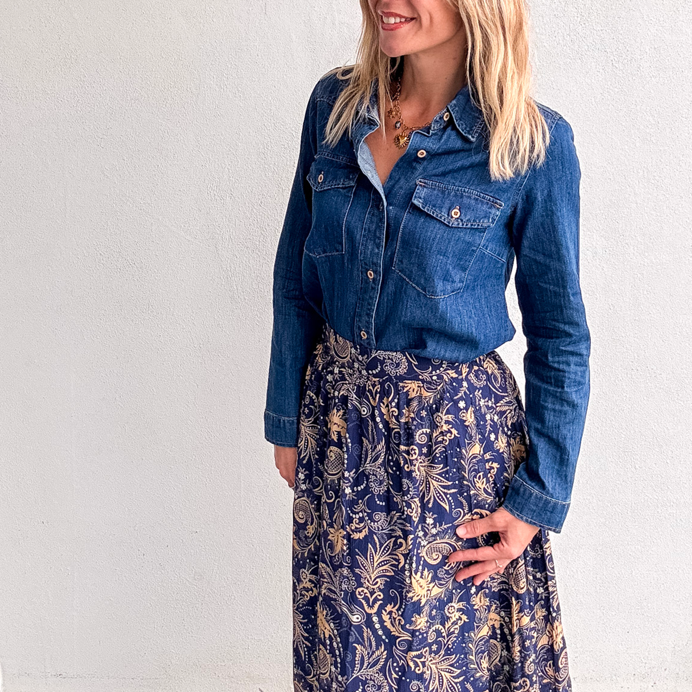 Jupe longue fluide motif cachemire bleu marine et or, portée avec une chemise en jean et des bottines noires.