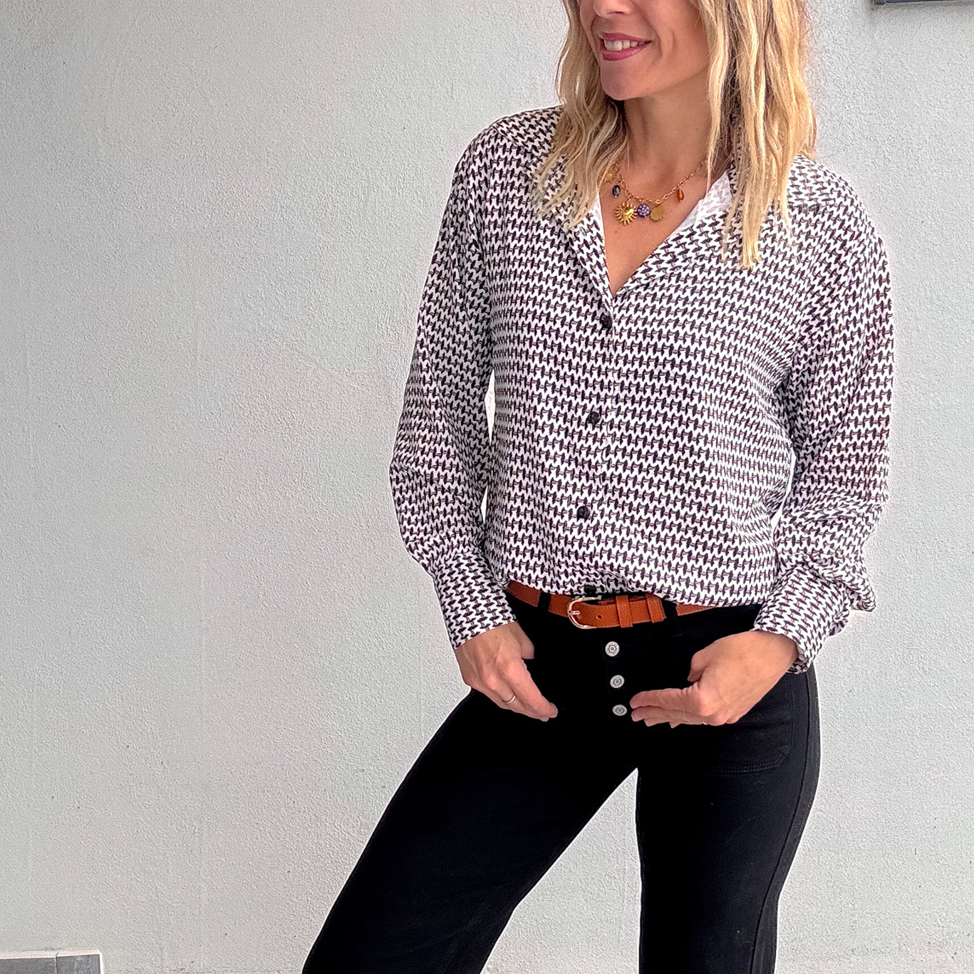 Chemise femme 100% polyester motif pied-de-poule noir et blanc, portée rentrée dans un jean noir taille haute avec une ceinture marron.