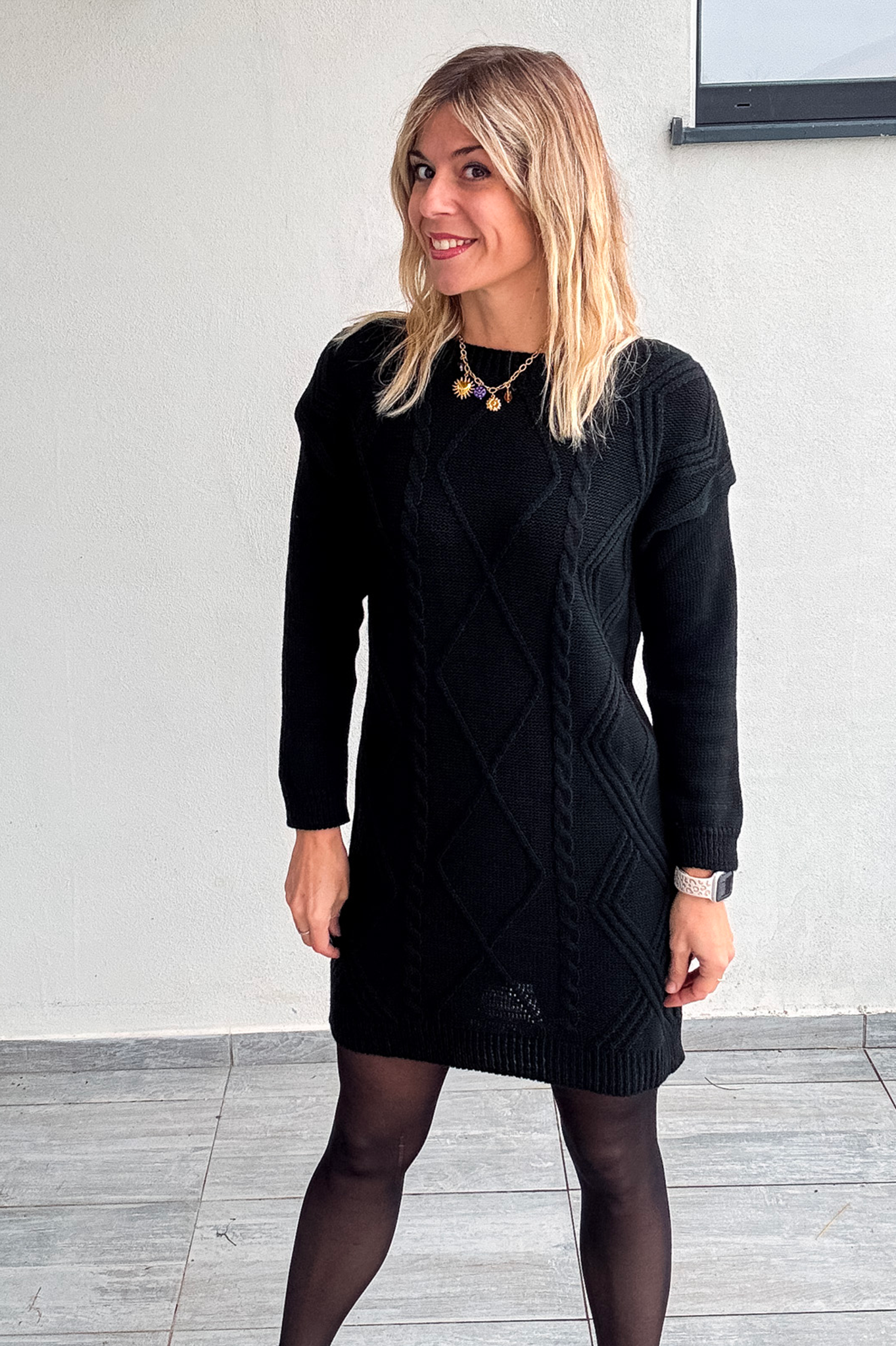 Robe pull courte noire en maille torsadée, des collants noirs et des bottines.