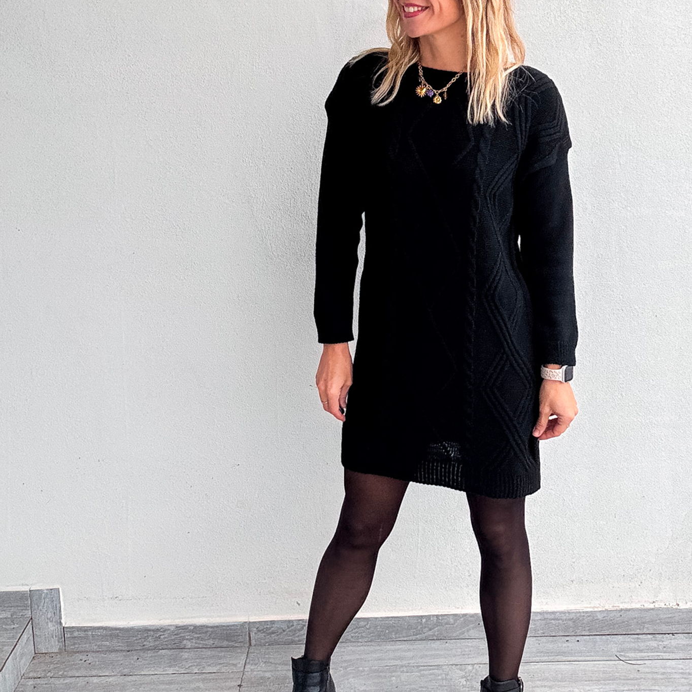 Robe pull courte noire en maille torsadée, des collants noirs et des bottines.