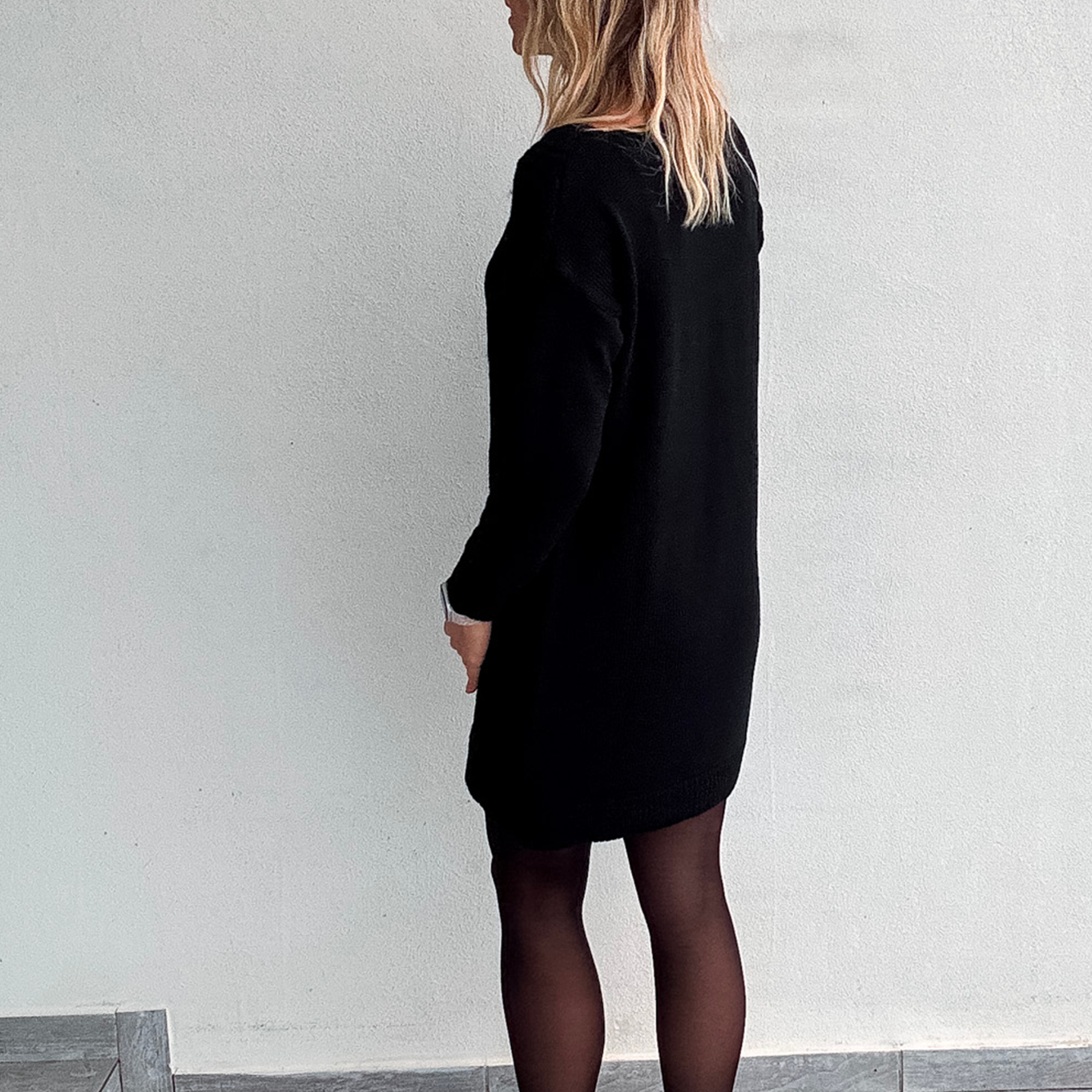 Robe pull courte noire en maille torsadée, des collants noirs et des bottines.
