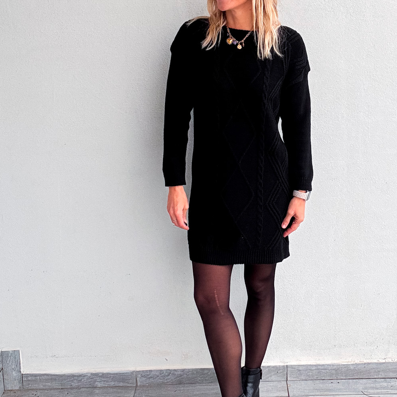 Robe pull courte noire en maille torsadée, des collants noirs et des bottines.