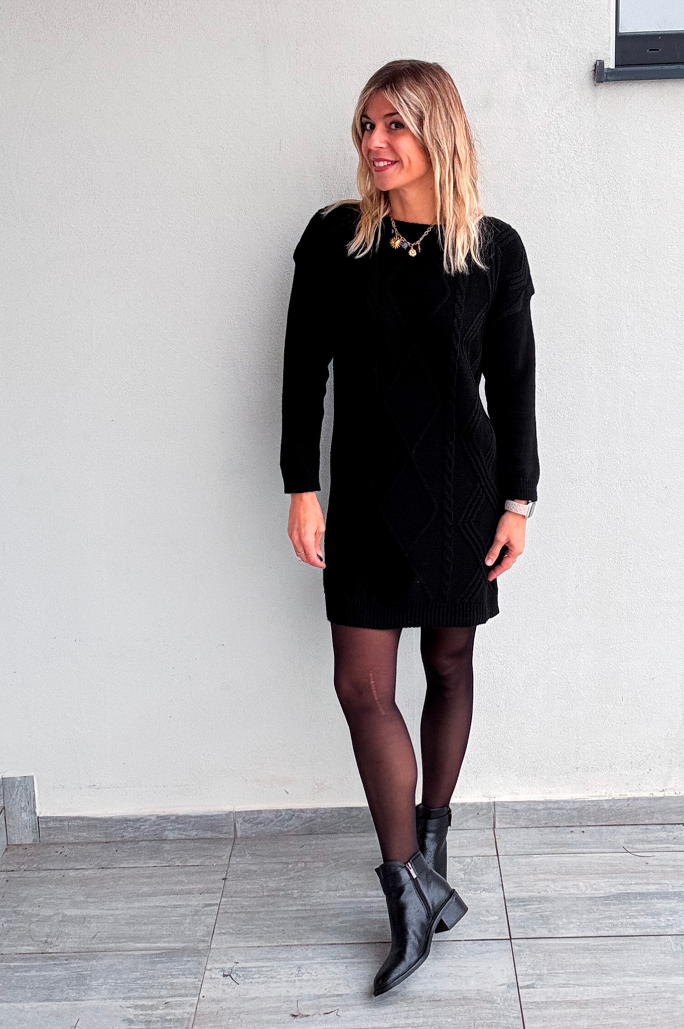 Robe pull courte noire en maille torsadée, des collants noirs et des bottines.