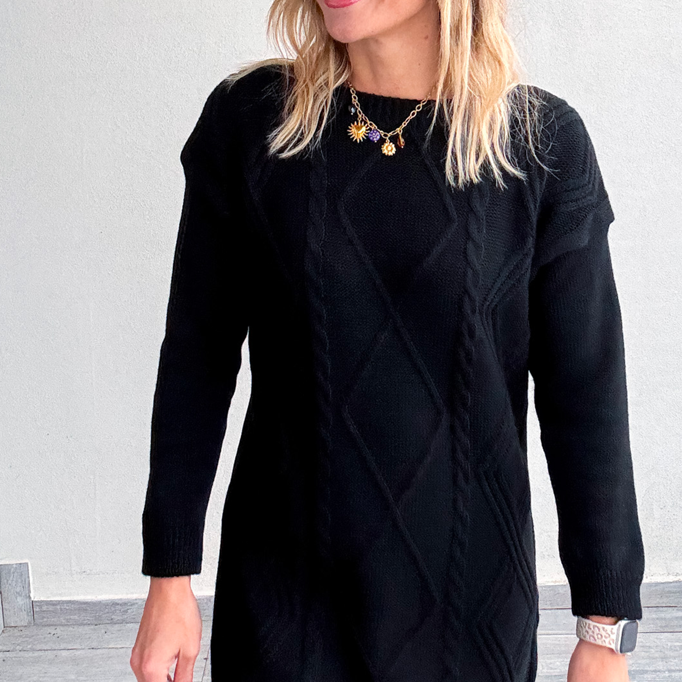 Robe pull courte noire en maille torsadée, des collants noirs et des bottines.