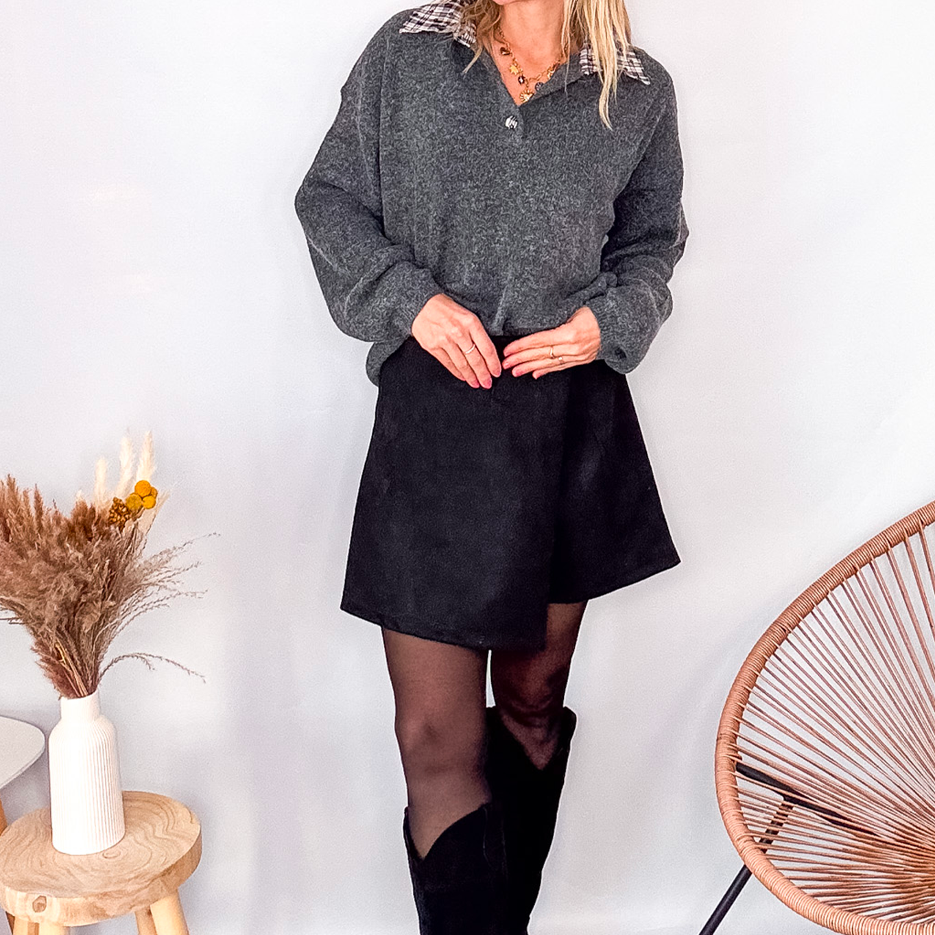 Pull gris chiné avec col en tissu imprimé carreaux, porté rentré dans une jupe noire suédine avec des collants opaques et des bottes.