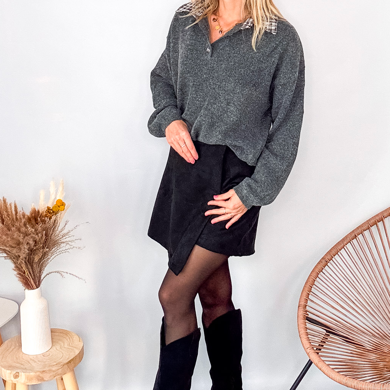Pull gris chiné avec col en tissu imprimé carreaux, porté rentré dans une jupe noire suédine avec des collants opaques et des bottes.