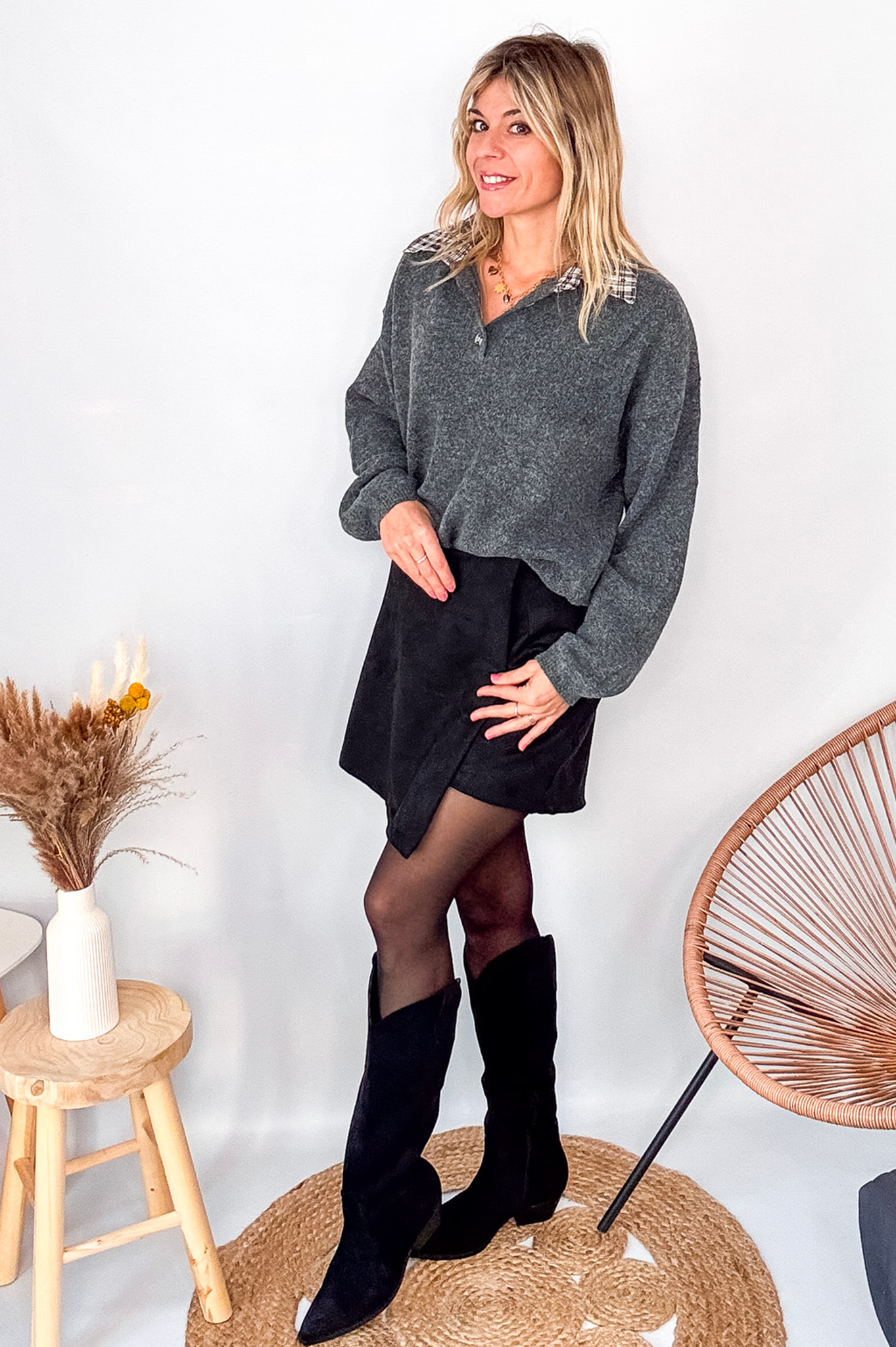 Pull gris chiné avec col en tissu imprimé carreaux, porté rentré dans une jupe noire suédine avec des collants opaques et des bottes.