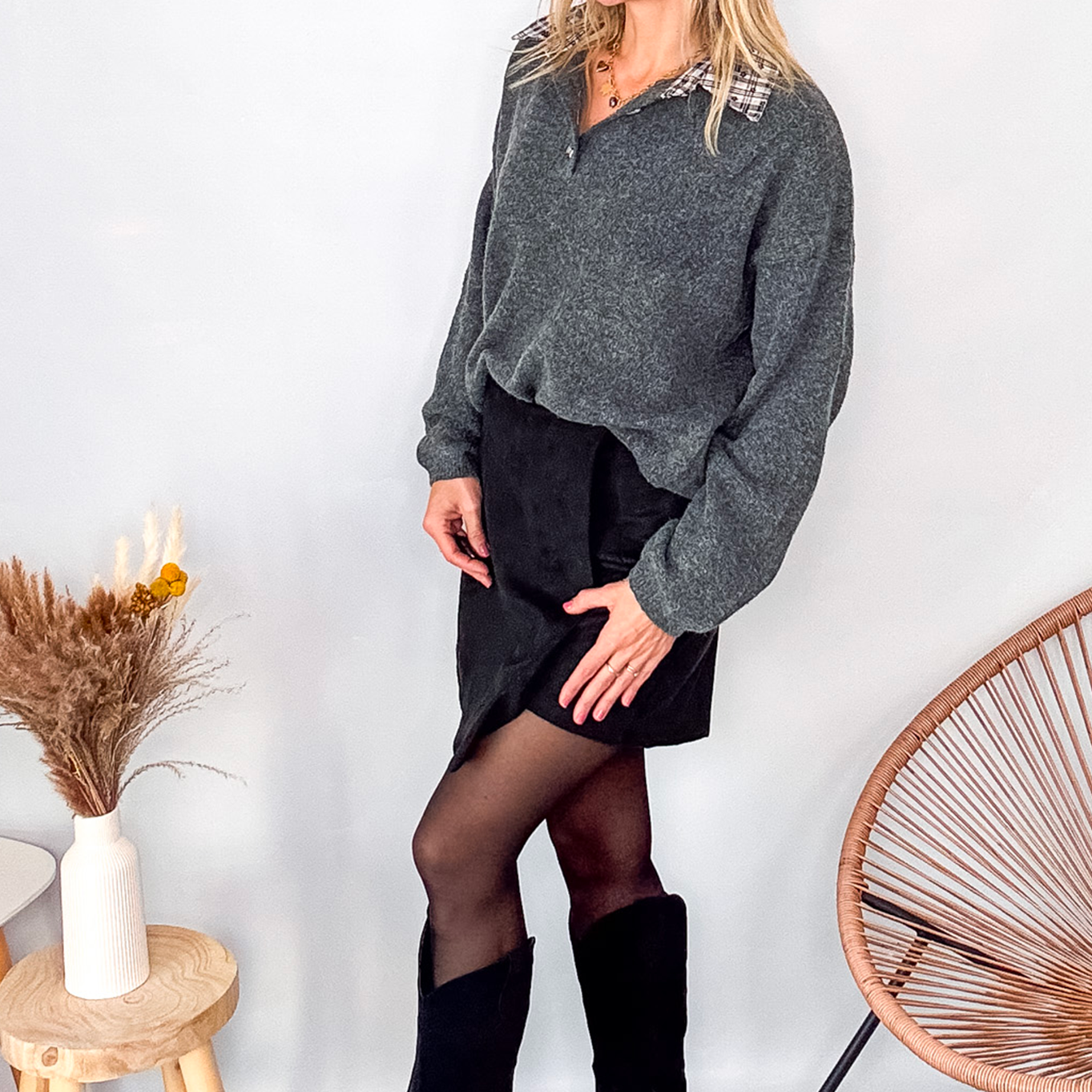 Pull gris chiné avec col en tissu imprimé carreaux, porté rentré dans une jupe noire suédine avec des collants opaques et des bottes.