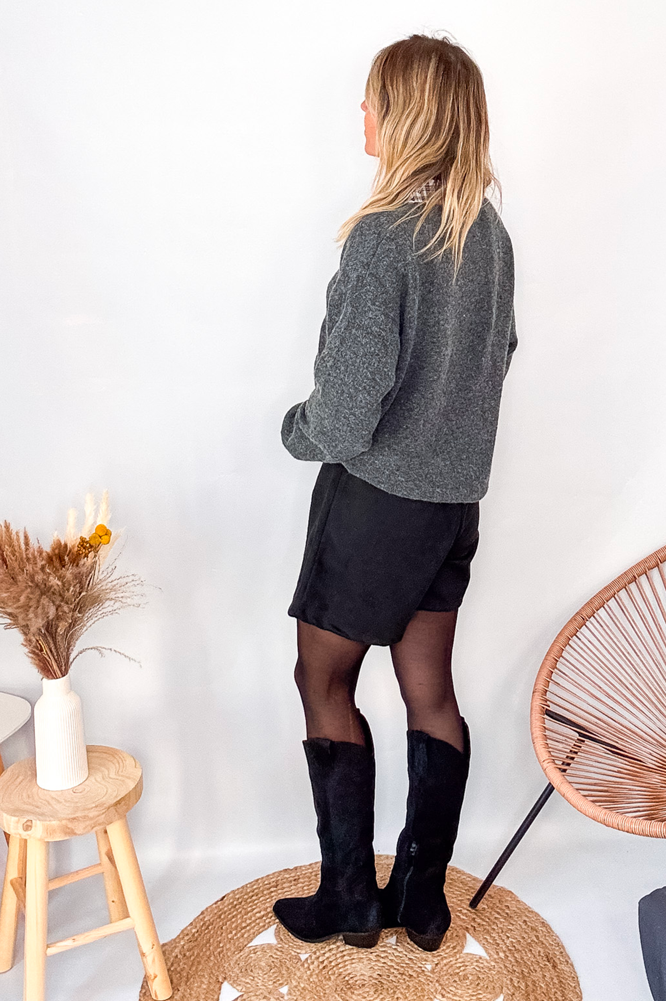 Pull gris chiné avec col en tissu imprimé carreaux, porté rentré dans une jupe noire suédine avec des collants opaques et des bottes.