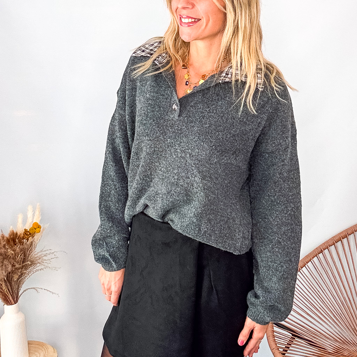 Pull gris chiné avec col en tissu imprimé carreaux, porté rentré dans une jupe noire suédine avec des collants opaques et des bottes.