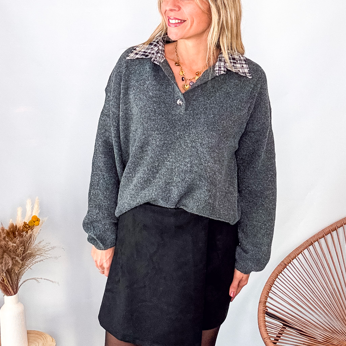 Pull gris chiné avec col en tissu imprimé carreaux, porté rentré dans une jupe noire suédine avec des collants opaques et des bottes.