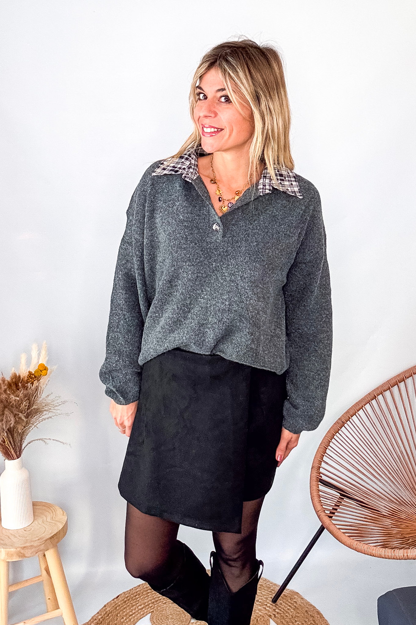 Pull gris chiné avec col en tissu imprimé carreaux, porté rentré dans une jupe noire suédine avec des collants opaques et des bottes.