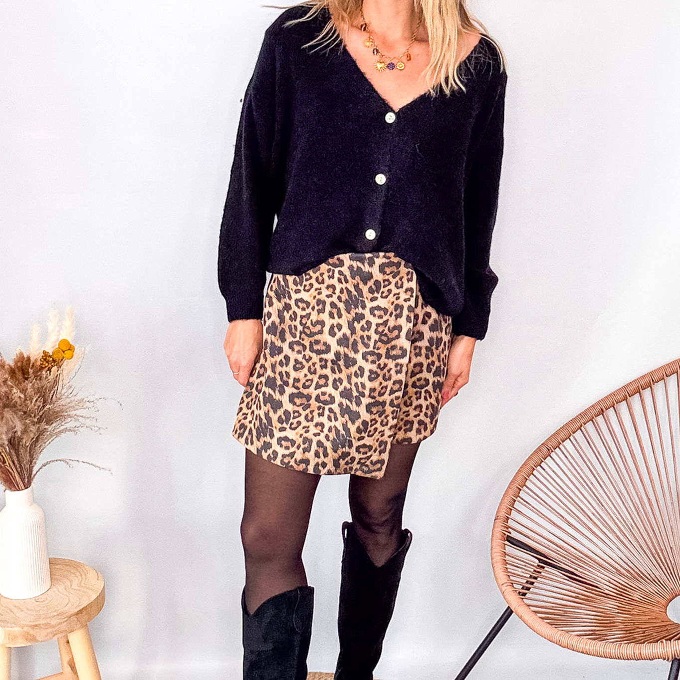 Gilet cardigan noir Baby Alpaga col V, porté sur une jupe courte imprimée léopard et des bottes noires hautes.