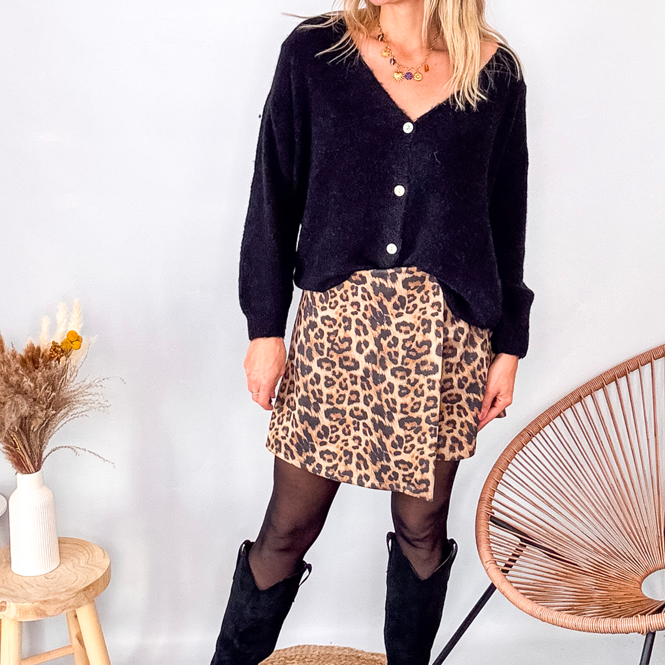 Gilet cardigan noir Baby Alpaga col V, porté sur une jupe courte imprimée léopard et des bottes noires hautes.