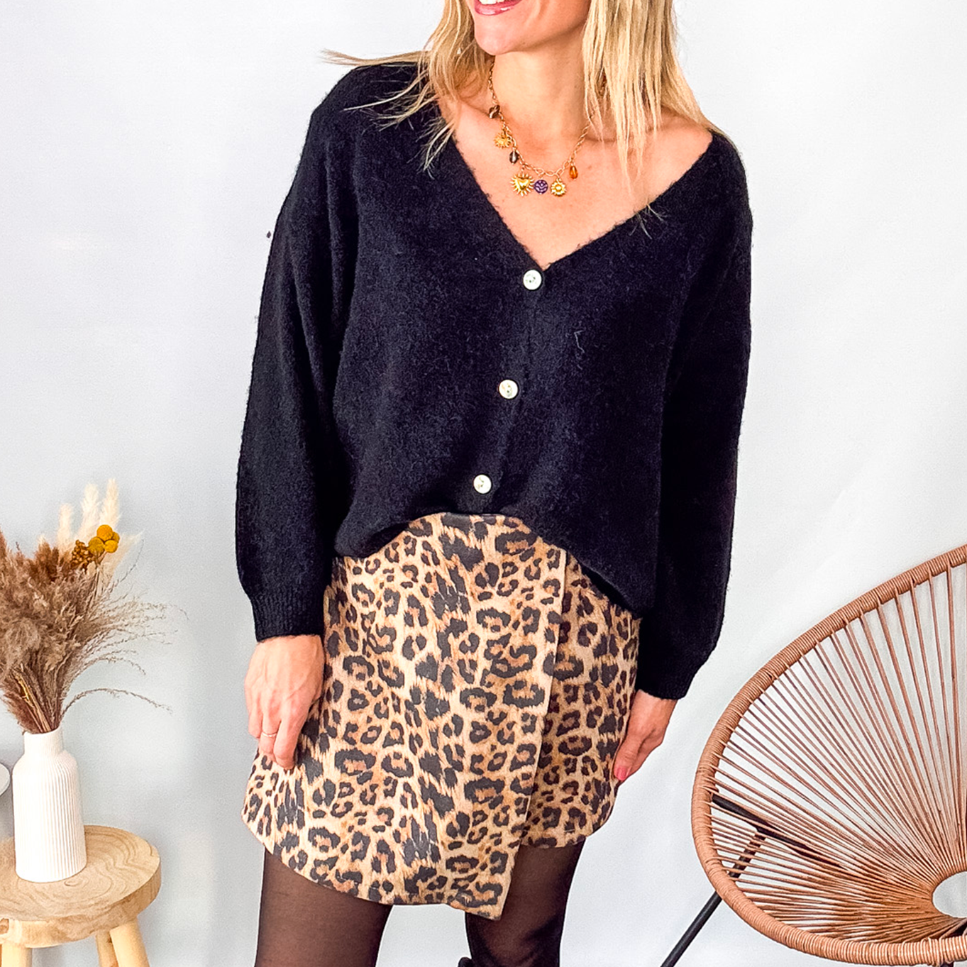 Gilet cardigan noir Baby Alpaga col V, porté sur une jupe courte imprimée léopard et des bottes noires hautes.