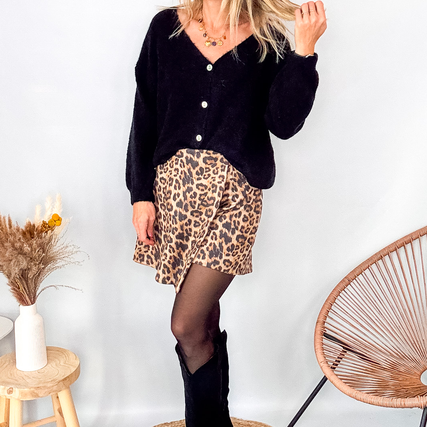 Gilet cardigan noir Baby Alpaga col V, porté sur une jupe courte imprimée léopard et des bottes noires hautes.