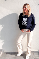 Pull bleu marine avec motif 'amour' cœur fleuri, boutons décoratifs sur l'épaule, porté avec un jean écru et des baskets blanches.