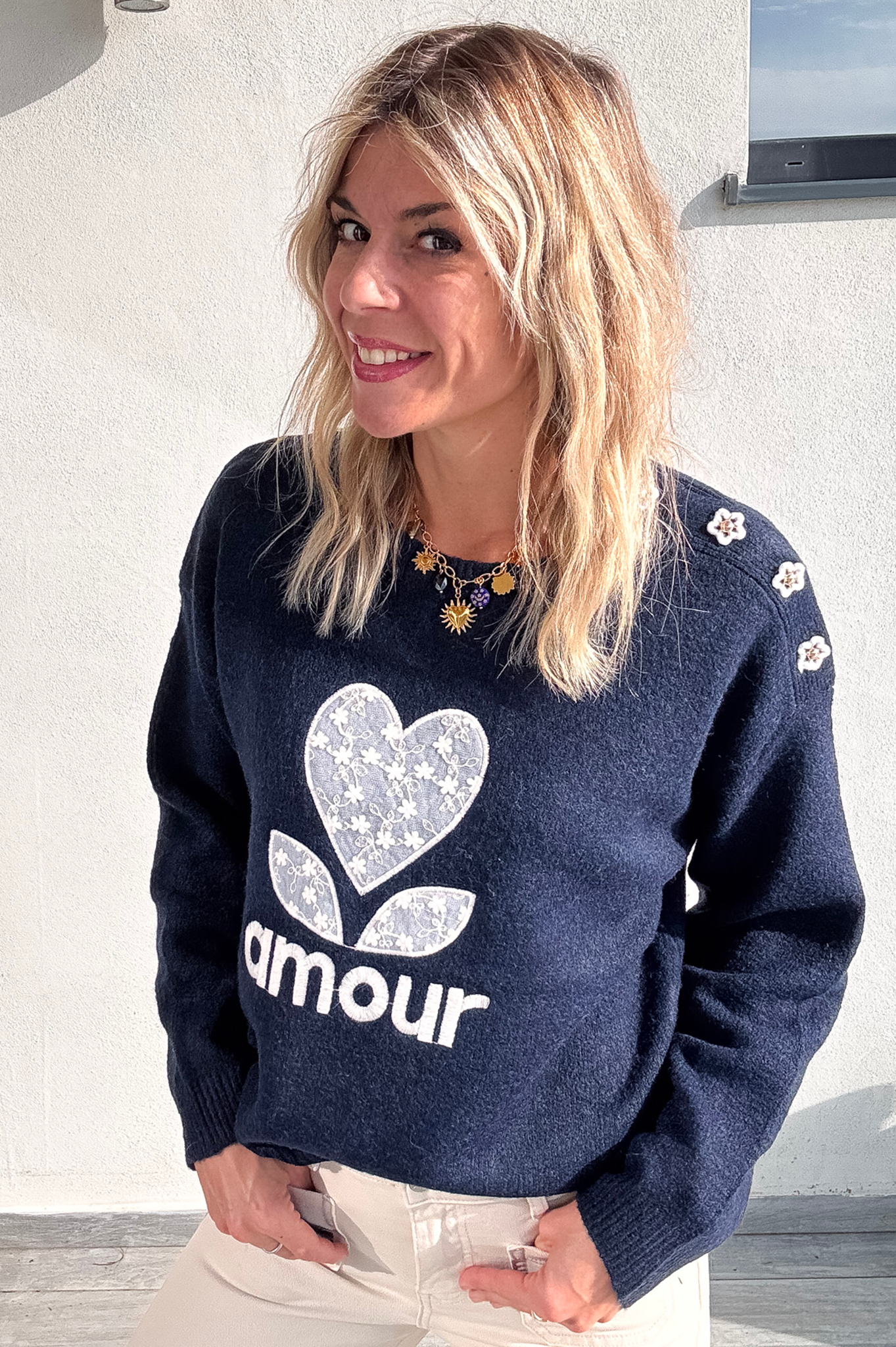 Pull bleu marine avec motif 'amour' cœur fleuri, boutons décoratifs sur l'épaule, porté avec un jean écru et des baskets blanches.