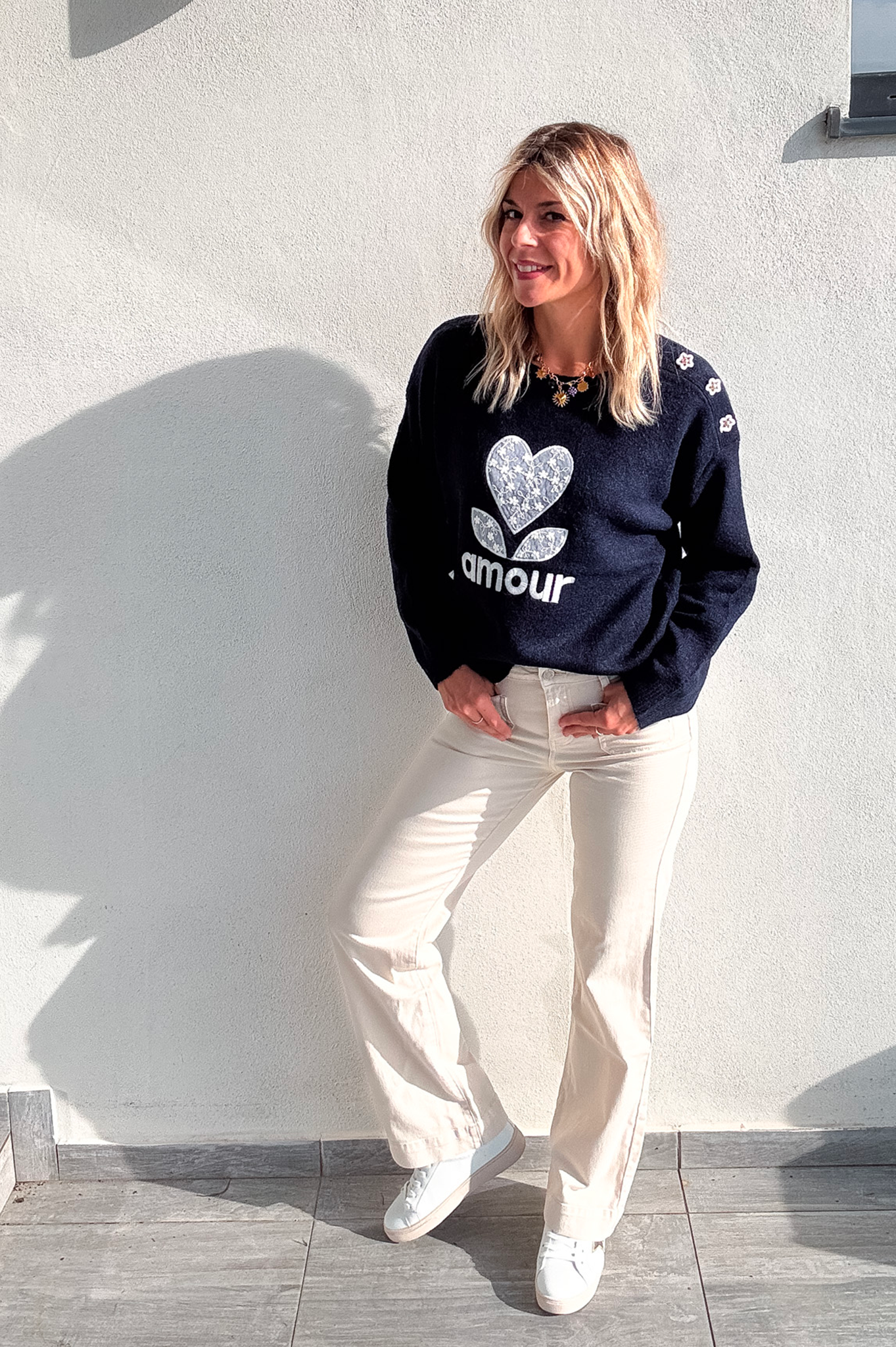 Pull bleu marine avec motif 'amour' cœur fleuri, boutons décoratifs sur l'épaule, porté avec un jean écru et des baskets blanches.