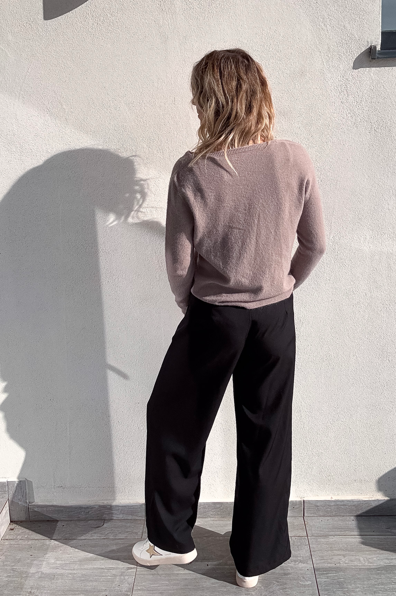 Pantalon large noir taille haute, coupe fluide, porté avec un pull taupe et des baskets blanches, look confortable et élégant.