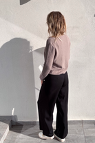 Pantalon large noir taille haute, coupe fluide, porté avec un pull taupe et des baskets blanches, look confortable et élégant.