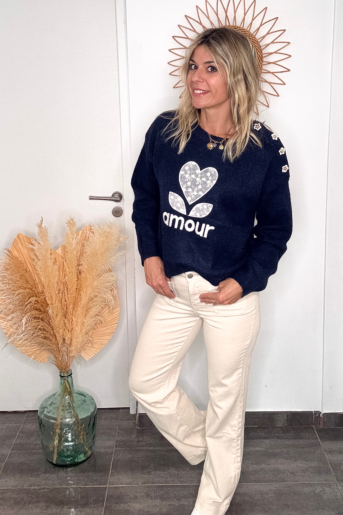 Pull bleu marine avec motif 'amour' cœur fleuri, boutons décoratifs sur l'épaule, porté avec un jean écru et des baskets blanches.