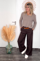 Pantalon tailleur marron chocolat, coupe large taille haute, porté avec un pull taupe, une ceinture camel et des baskets blanches.