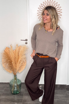 Pantalon tailleur marron chocolat, coupe large taille haute, porté avec un pull taupe, une ceinture camel et des baskets blanches.