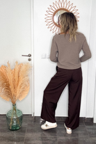 Pantalon tailleur marron chocolat, coupe large taille haute, porté avec un pull taupe, une ceinture camel et des baskets blanches.