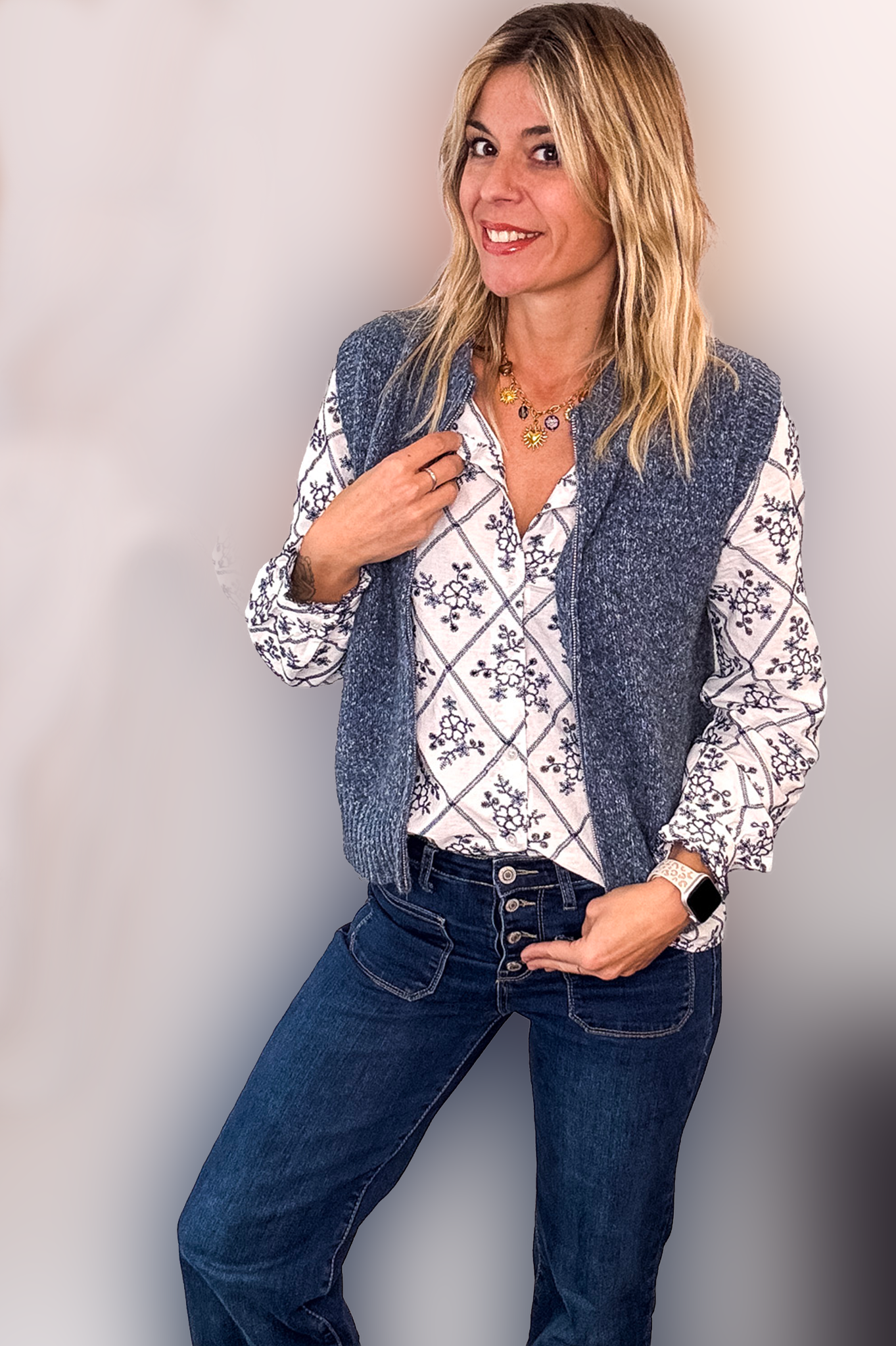 Gilet sans manches zippé bleu denim en maille tressée, col montant, porté sur une chemise à motifs et un jean flare.