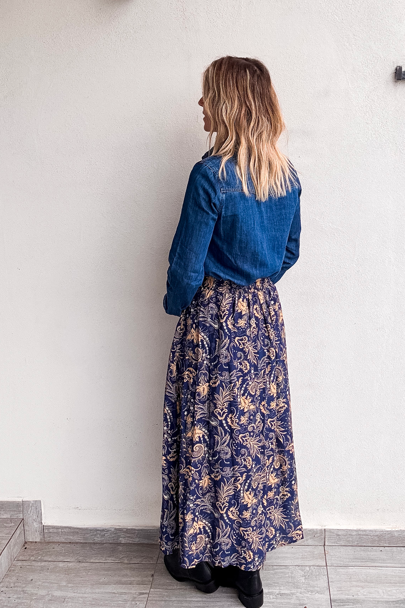 Jupe longue fluide motif cachemire bleu marine et or, portée avec une chemise en jean et des bottines noires.