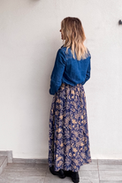 Jupe longue fluide motif cachemire bleu marine et or, portée avec une chemise en jean et des bottines noires.