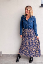 Jupe longue fluide motif cachemire bleu marine et or, portée avec une chemise en jean et des bottines noires.