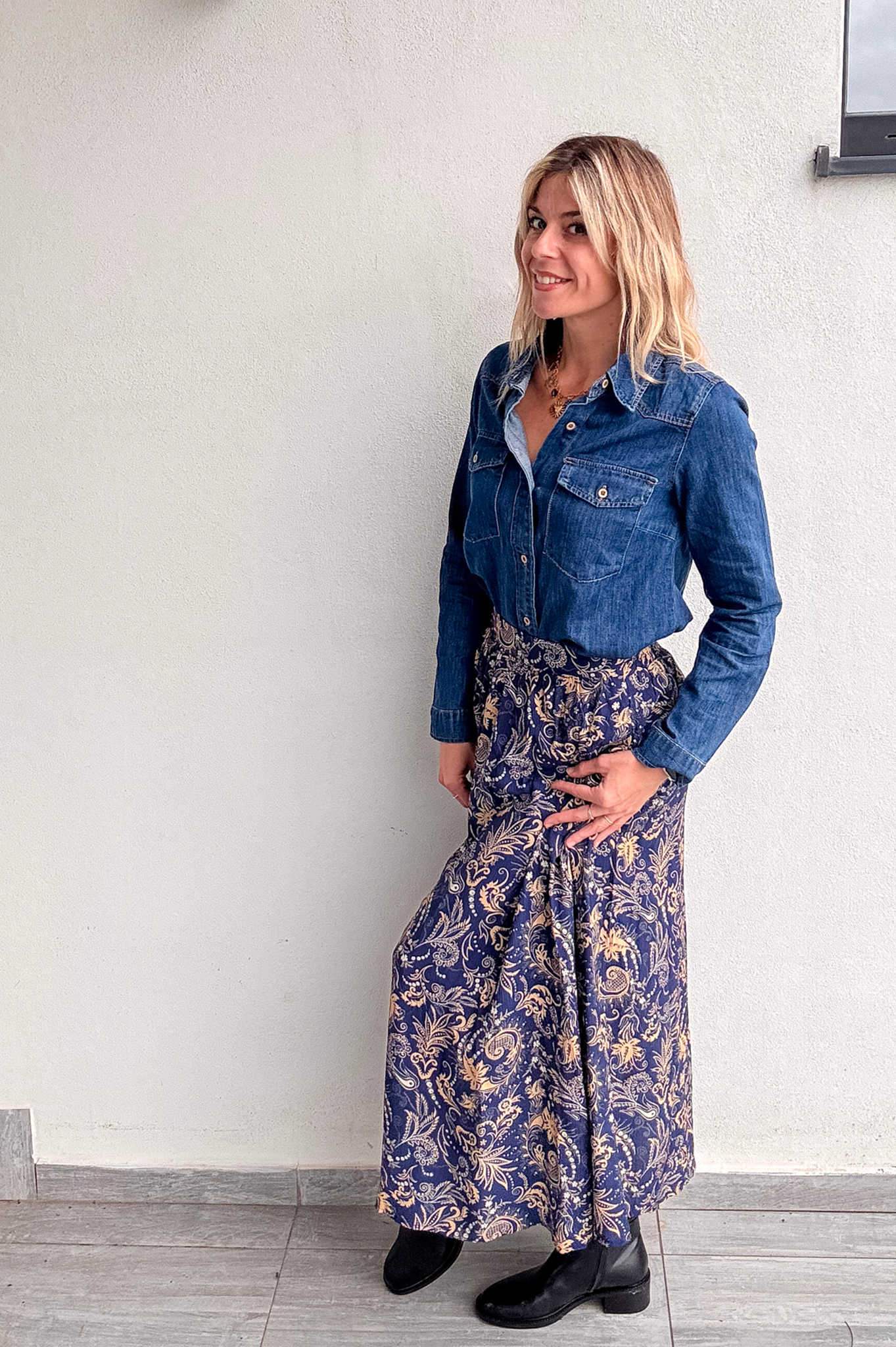 Jupe longue fluide motif cachemire bleu marine et or, portée avec une chemise en jean et des bottines noires.