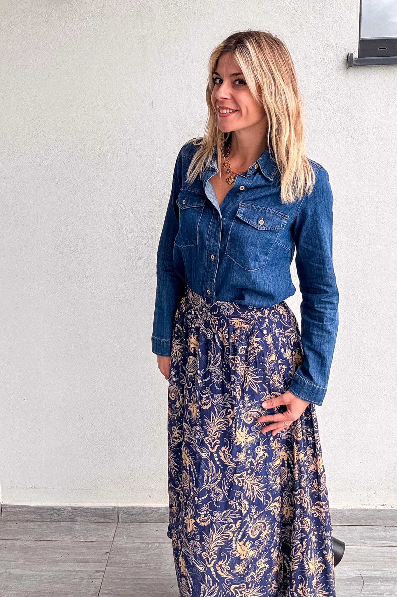 Jupe longue fluide motif cachemire bleu marine et or, portée avec une chemise en jean et des bottines noires.