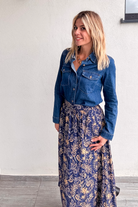 Jupe longue fluide motif cachemire bleu marine et or, portée avec une chemise en jean et des bottines noires.