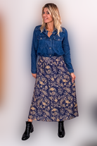 Jupe longue fluide motif cachemire bleu marine et or, portée avec une chemise en jean et des bottines noires.