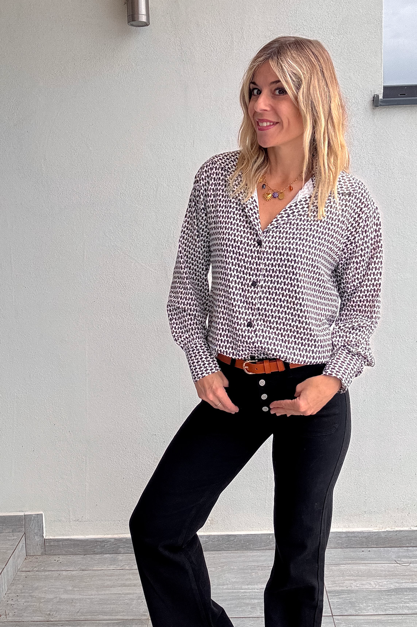 Chemise femme 100% polyester motif pied-de-poule noir et blanc, portée rentrée dans un jean noir taille haute avec une ceinture marron.