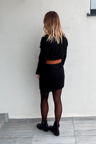 Robe pull courte noire en maille torsadée, portée avec une large ceinture marron, des collants noirs et des bottines.