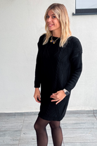 Robe pull courte noire en maille torsadée, des collants noirs et des bottines.