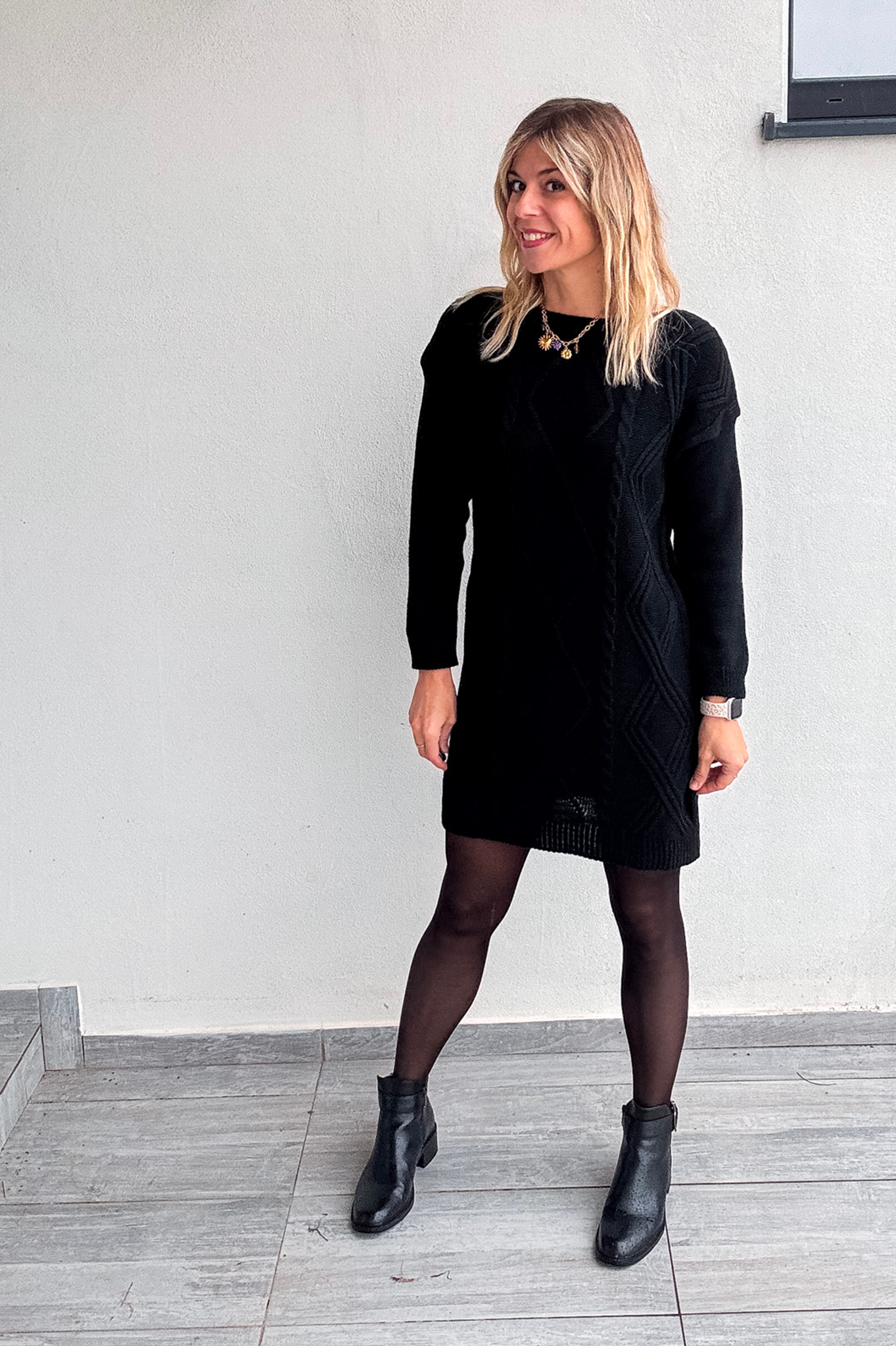 Robe pull courte noire en maille torsadée, des collants noirs et des bottines.