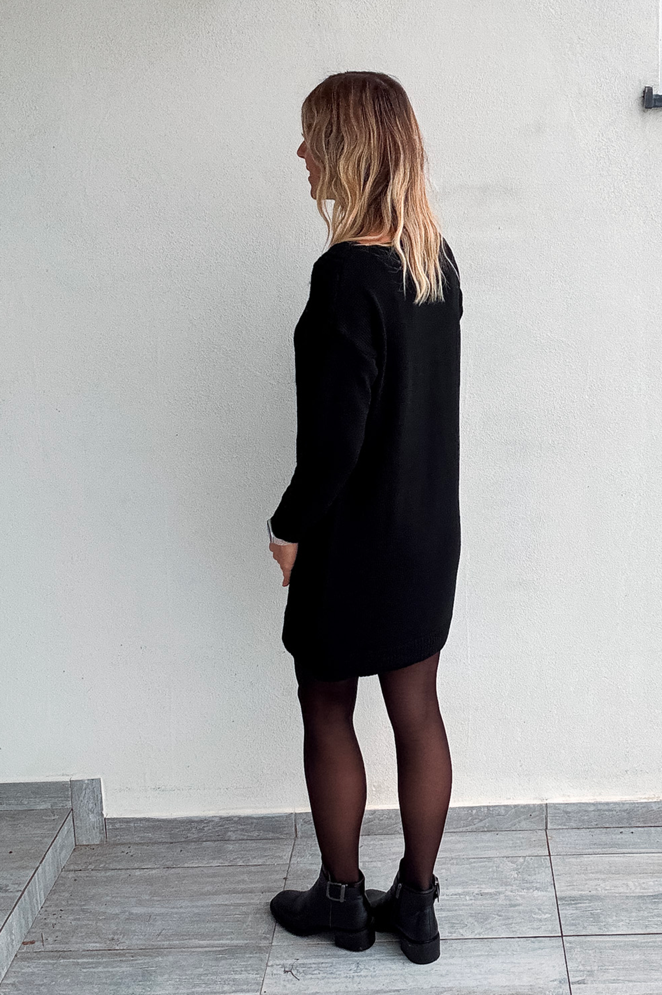 Robe pull courte noire en maille torsadée, des collants noirs et des bottines.